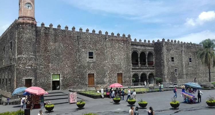 Los visitantes exploran un gran palacio tipo fortaleza de piedra con balcones arqueados y muros almenados.