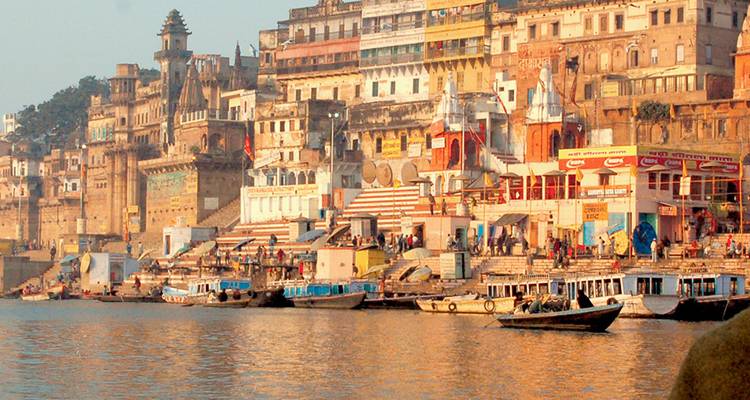 Goudkleurige oevers van de rivier in Varanasi met tempels, huizen en aangemeerde boten.