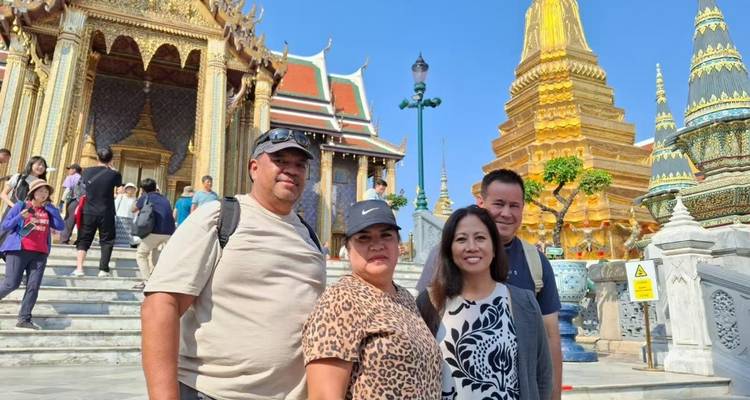 Quatre touristes posant sur les marches du Grand Palais de Bangkok avec des stupas dorés et des salles ornées à l'arrière-plan.