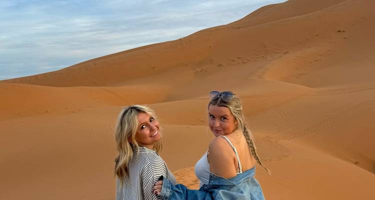 Dos amigos sonriendo mientras están de pie en las dunas de arena naranja ondulantes del Desierto del Sahara.