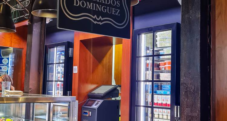 Intérieur d'un marché gastronomique moderne avec des vitrines réfrigérées, des luminaires suspendus et un petit comptoir bar.