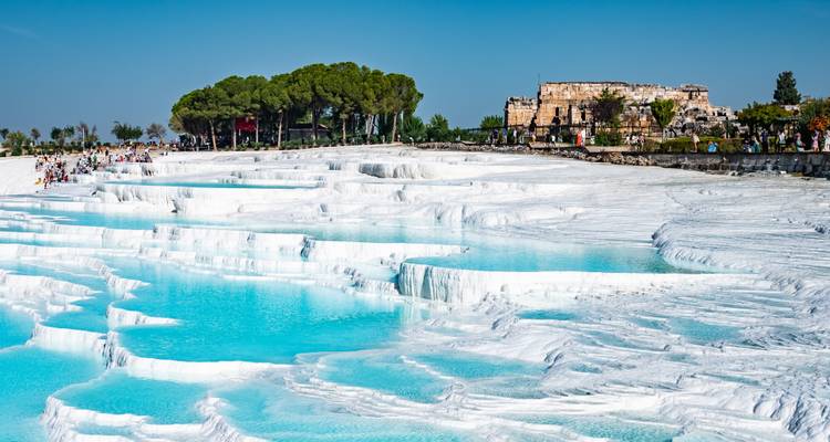 Des bassins thermaux d'un bleu turquoise éclatant s'écoulant en cascades sur des terrasses de travertin blanc, avec des visiteurs marchant le long des bords.