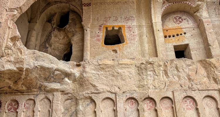 Gros plan de la façade d'une église rupestre ancienne avec des niches cintrées et des fresques rouges fanées gravées dans la pierre tendre.