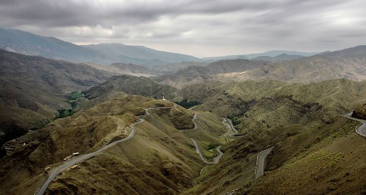 Dramatic aerial perspective of a winding mountain road snaking through barren Atlas peaks under moody skies.