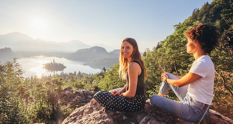 Twee vrienden ontspannen op een rotsachtig uitkijkpunt boven het Meer van Bled met zijn eilandkerk bij zonsopgang.