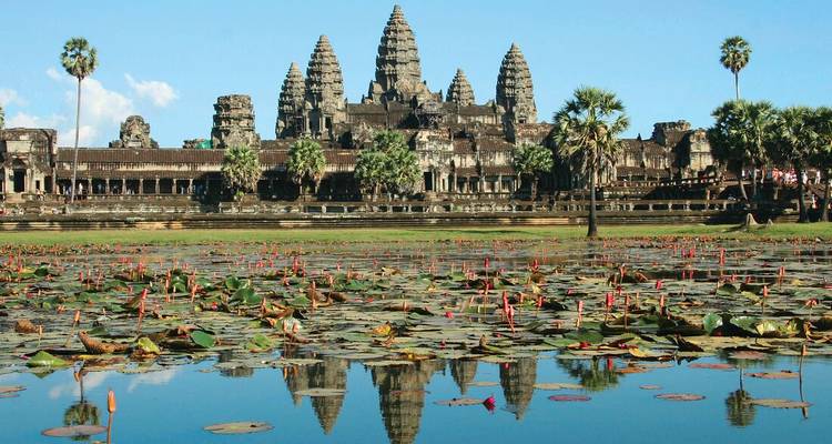 Classic panorama of Angkor Wat reflected in a lotus-filled moat under a clear blue sky.
