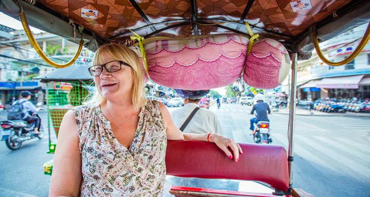 Smiling traveller rides in a tuk-tuk through busy city streets.