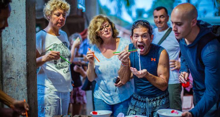 Touristen kosten enthusiastisch Nudeln von einem Straßenstand, ein Mann schlürft dramatisch