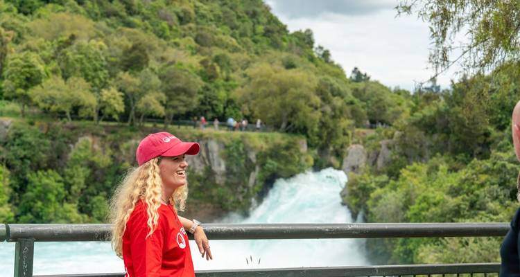 Smiling traveler in red cap stands by railing overlooking powerful turquoise waterfall