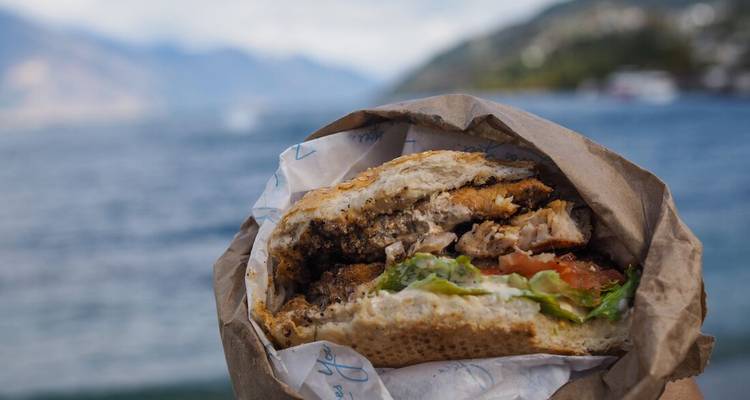 Close-up of a gourmet burger held with a scenic lake and mountains in the background