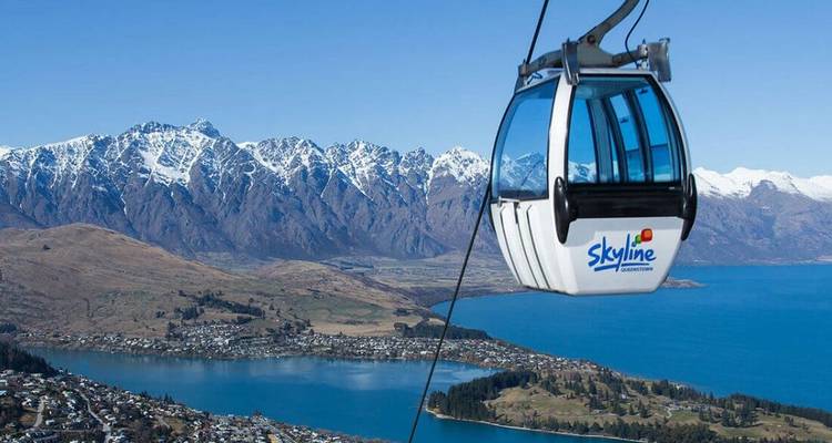 Skyline gondola cabin ascending above a lake and snow-capped mountain range