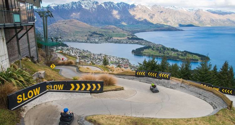 Winding luge track on a hillside overlooking a town and blue lake far below