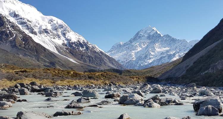 Rocky glacier riverbed with snowy alpine peaks against a clear blue sky