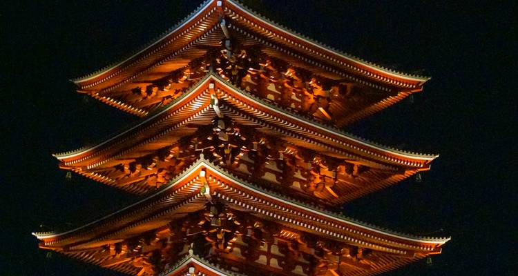 Vue rapprochée nocturne d'une pagode à plusieurs étages chaleureusement illuminée contre le ciel sombre, mettant en évidence les avant-toits en bois complexes.