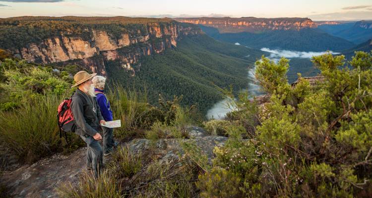 Dos excursionistas observando acantilados espectaculares y valles llenos de neblina en las Montañas Azules de Australia al amanecer.