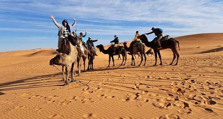 Des voyageurs chevauchant une file de chameaux à travers les dunes désertiques dorées sous un ciel bleu