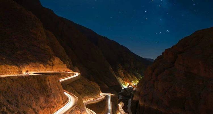 Photographie en pose longue de nuit d'une route de montagne sinueuse dans les Gorges du Dadès sous un ciel étoilé.