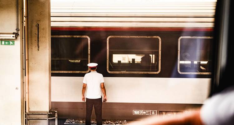 Un chef de train en uniforme blanc se tient sur le quai face à une voiture.