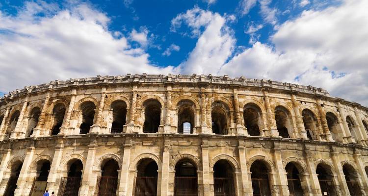 Vue grand angle de l'ancienne Arène romaine de Nîmes se détachant sur un ciel bleu vibrant.