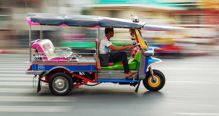 Kleurrijke tuk-tuk die met bewegingsonscherpte door een stadsstraat raast.