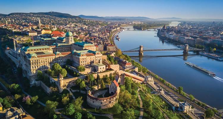 Vista aérea del amanecer sobre Budapest mostrando el Castillo de Buda, el Puente de las Cadenas y el Danubio serpentando a través de la ciudad.