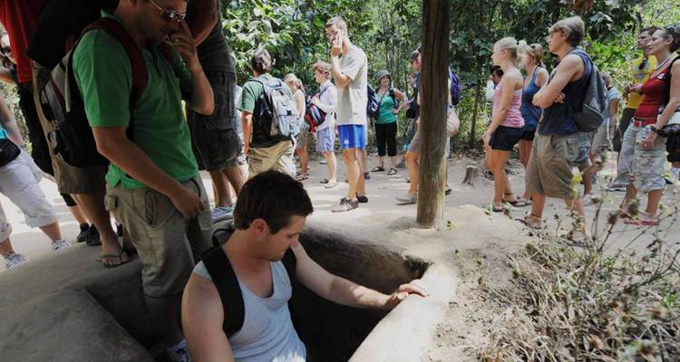 Toergroep verzameld rond een smalle ingang bij de historische Cu Chi Tunnels, met een man die naar binnen klimt.