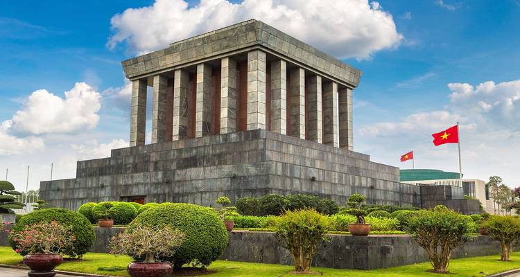 Het indrukwekkende granieten Ho Chi Minh Mausoleum met daarvoor verzorgde tuinen en de Vietnamese vlag onder blauwe lucht.