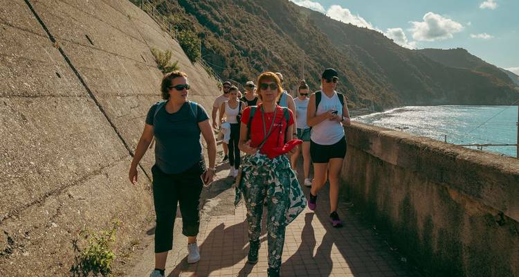 Eine Wandergruppe läuft auf einem Küstenpfad mit Blick auf türkisfarbene Gewässer und raue Hügel der Cinque Terre.