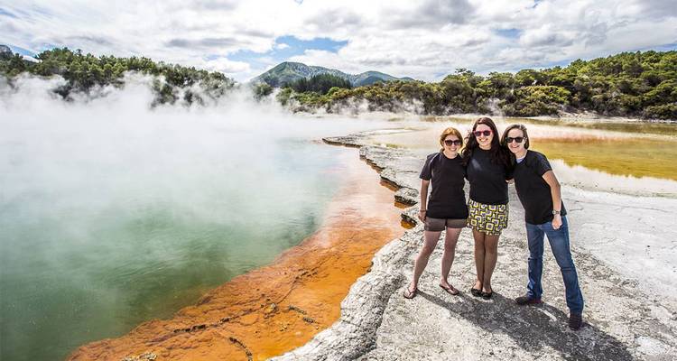 Drei Freunde posieren neben dem farbenfrohen geothermischen Champagne Pool mit aufsteigendem Dampf in Rotorua.