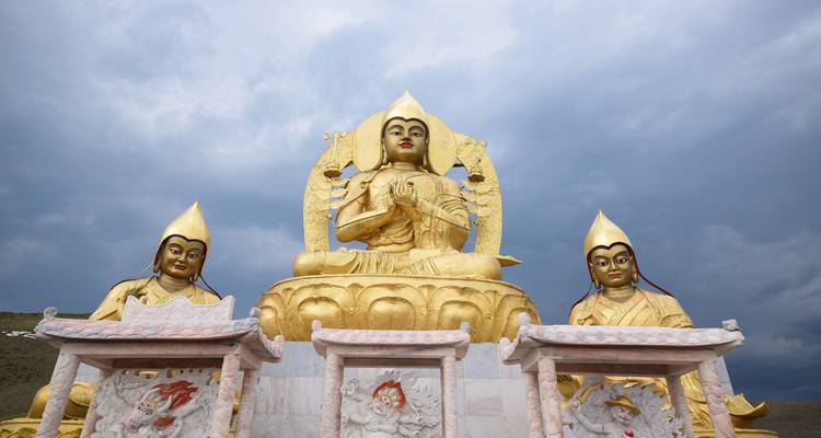 Drei monumentale goldene Buddha-Statuen sitzen unter einem dramatischen bewölkten Himmel in der Mongolei.