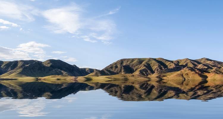 Ein stiller See spiegelt die grün-braunen mongolischen Berge unter einem klaren Himmel vollkommen wider.