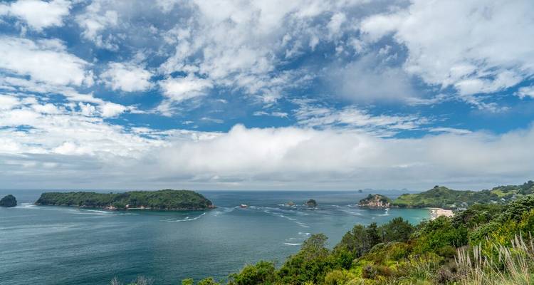 Une vue panoramique côtière d'îles émeraude et de mer turquoise sous un ciel parsemé de nuages blancs.