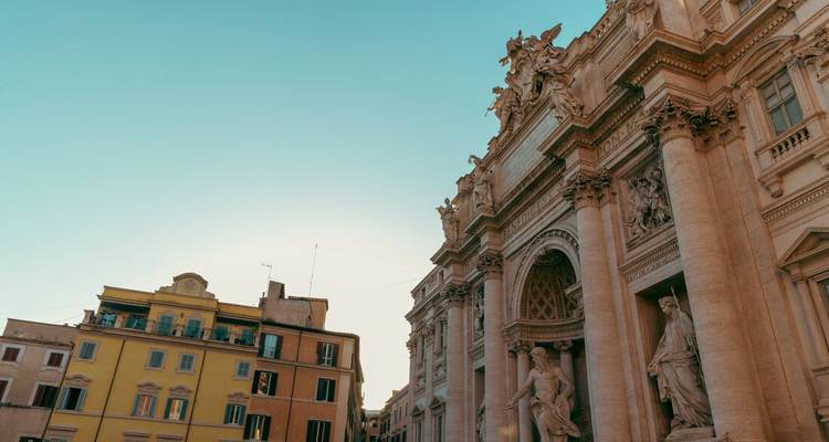 La façade en pierre ouvragée et les statues de la Fontaine de Trevi brillent chaleureusement sous un ciel bleu dégagé.
