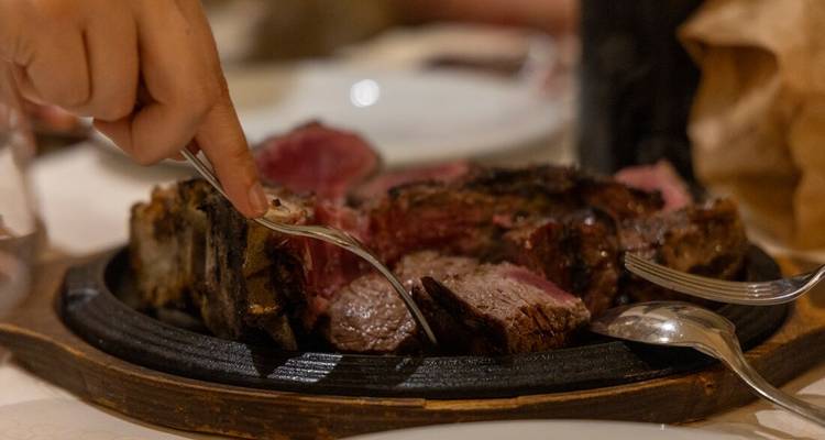Gros plan d'un plateau en bois grésillant contenant un steak grillé saignant en train d'être tranché à une table de restaurant.