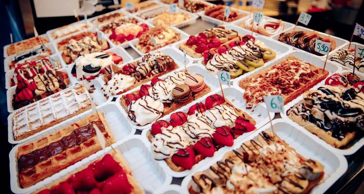 Des plateaux d'exposition empilés haut avec une assortiment de gaufres belges garnies de fruits, de chocolat et de crème.