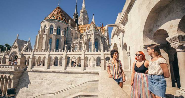 Des amis discutant à la Bastille des Pêcheurs à Budapest avec de magnifiques tours néo-gothiques ornées en arrière-plan.