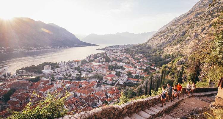 Les randonneurs montent des marches en pierre surplombant la ville aux toits rouges et la baie de Kotor au lever du soleil.