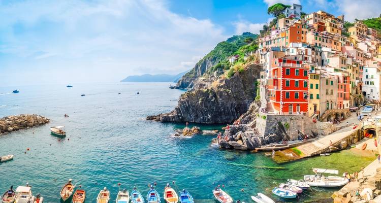 Vue panoramique du village coloré de Riomaggiore s'étalant en cascade le long des falaises rocheuses vers la mer bleue cristalline.