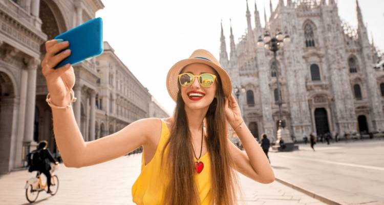 Jeune femme souriante prenant un selfie devant le Duomo orné de Milan par une belle journée