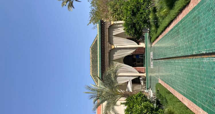 Symmetrical green-tiled walkway leads to an open pavilion framed by palms and manicured shrubs.