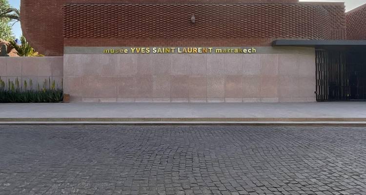 Modern brick facade of the Musée Yves Saint Laurent Marrakech with gold lettering against a cobbled street.