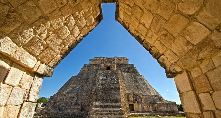 De stenen boog omlijst de indrukwekkende Pyramid of the Magician in Uxmal onder een helder blauwe lucht.