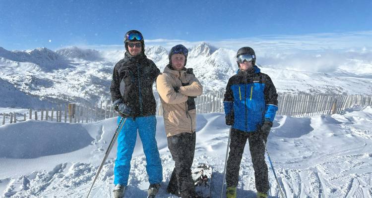 Trois skieurs posant sur une crête de montagne enneigée avec des bâtons de ski et des pics panoramiques.