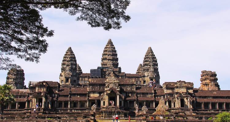 Iconisch frontaal uitzicht op de centrale torens van Angkor Wat, omlijst door takken tegen een heldere lucht.