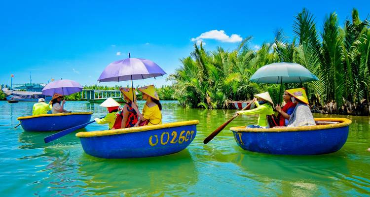Tourists wearing conical hats ride colorful round basket boats on a bright green river under blue sky.