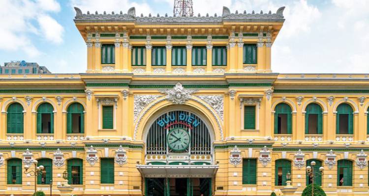 French colonial Central Post Office with yellow facade, arched windows and large clock.