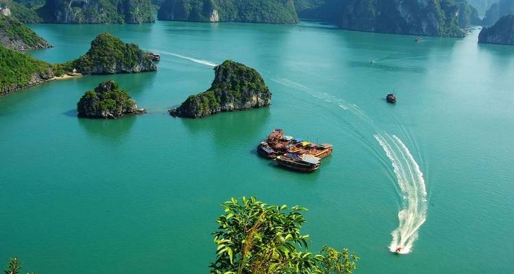 Turquoise waters of Halong Bay with scattered karst islets and boats leaving white wakes.