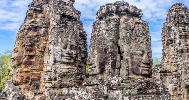 Ancient stone faces carved on towering Bayon temple pillars against a blue sky.