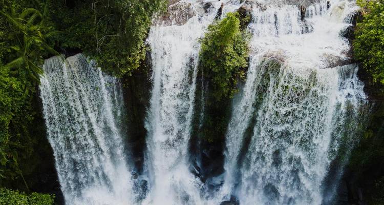 Powerful multi-tiered waterfall cascading between dense green jungle walls.