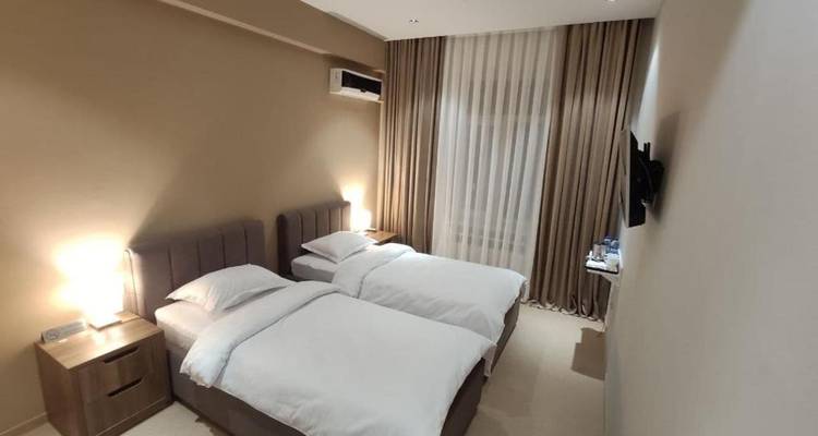 Einfaches modernes Hotelzimmer mit zwei Betten in Beige, zwei Einzelbetten, Nachttischlampen und neutraler Einrichtung.